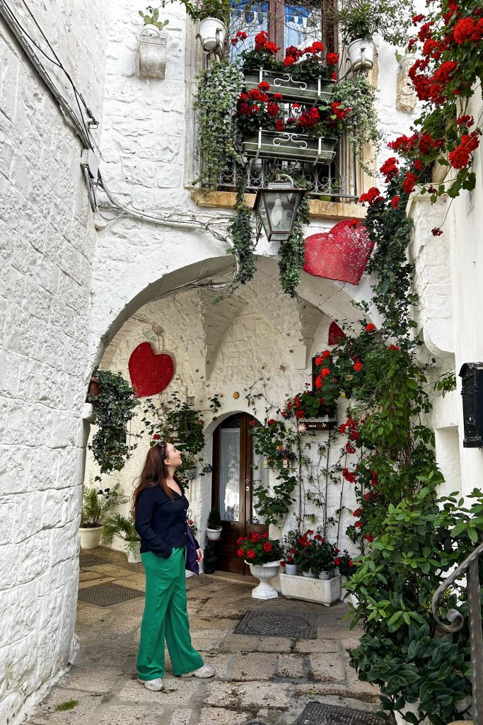 moi devant les façades blanches aux fleurs rouges du village de Cisternino dans les Pouilles en Italie
