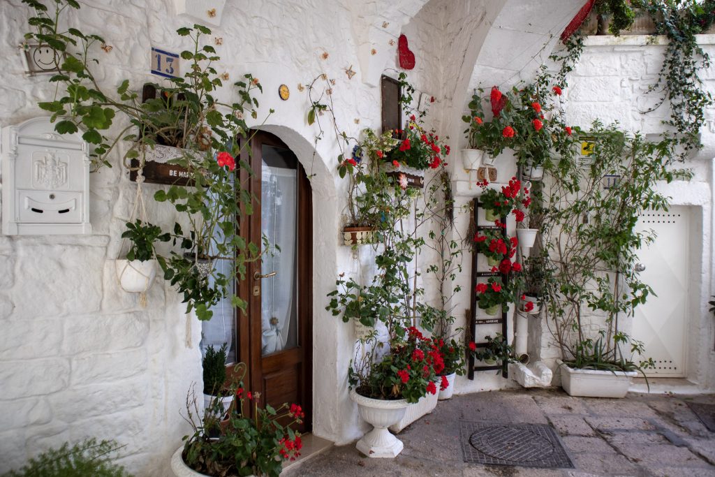 Façade blanche aux fleurs rouges dans le village de Cisternino